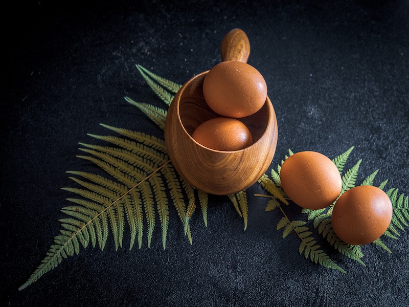 Brown eggs in a wooden mug on top of fern leaves.